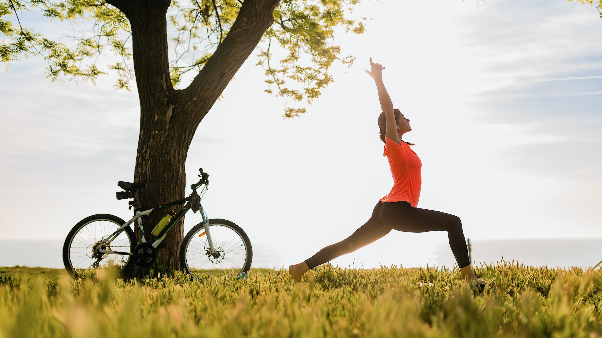 slim beautiful woman silhouette doing sports in morning in park doing yoga on mat in colorful fitness outfit in nature, smiling happy healthy lifestyle, calm meditation, bicycle on background